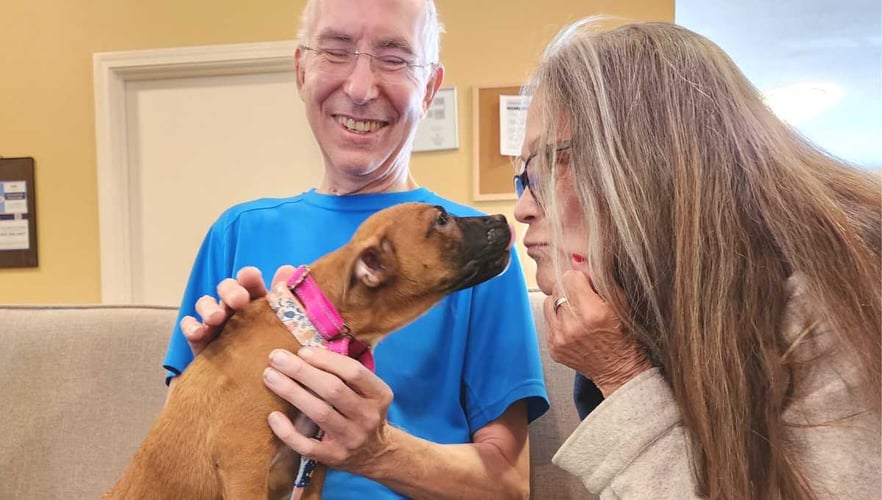 residents of pacifica senior living enjoy kisses with a pet therapy puppy